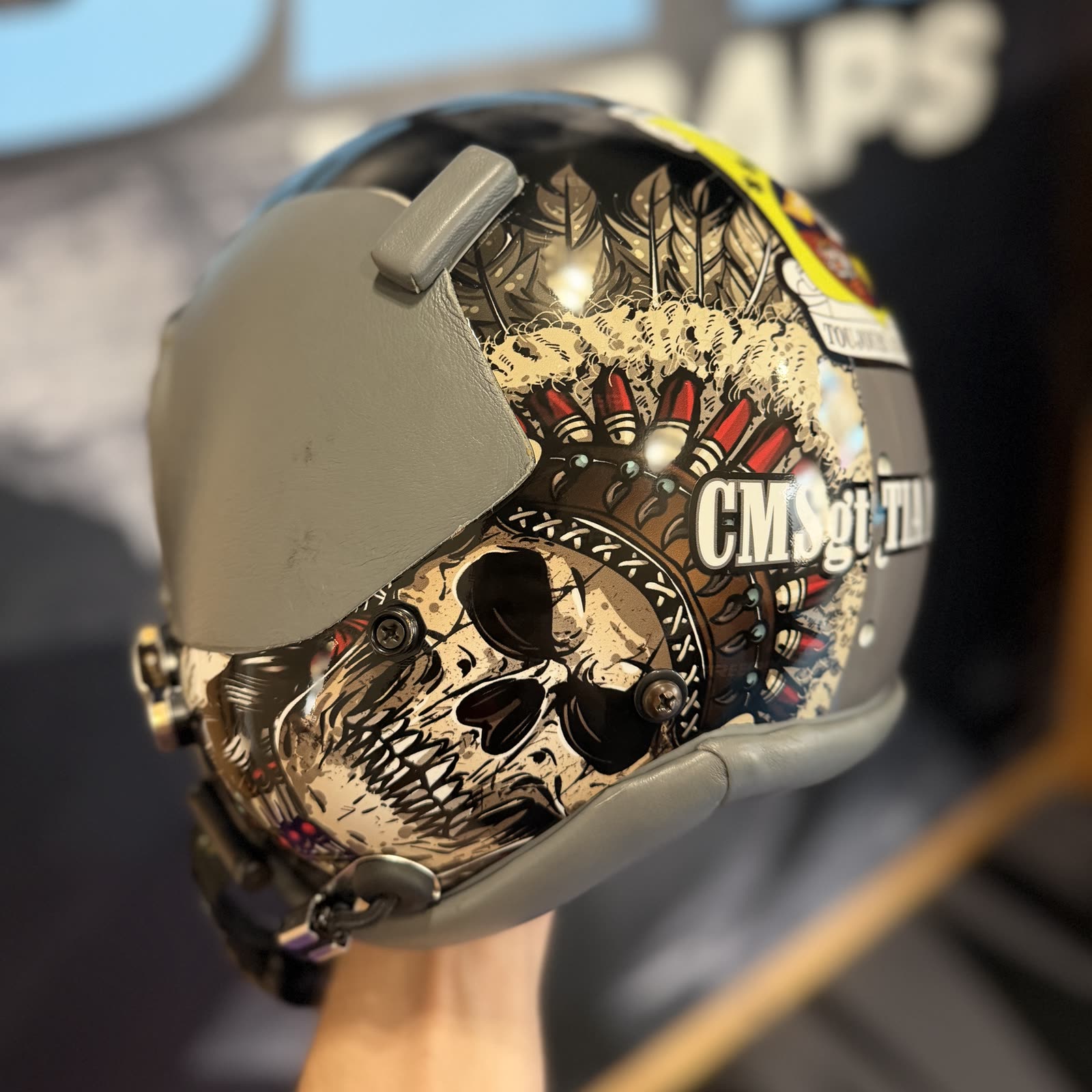 Close view of a helmet with tan, black, and red skull and feather artwork, with its visor and hardware visible.