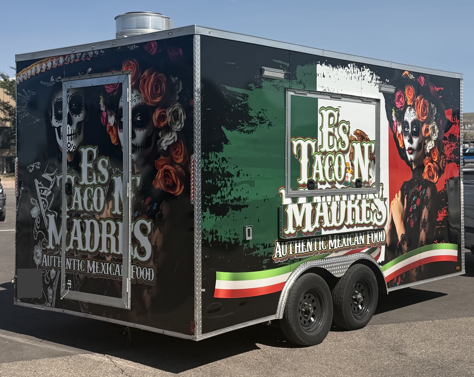 Enclosed food trailer with green, white, red and black graphics and floral and skull-themed artwork across its visible side and rear panels
