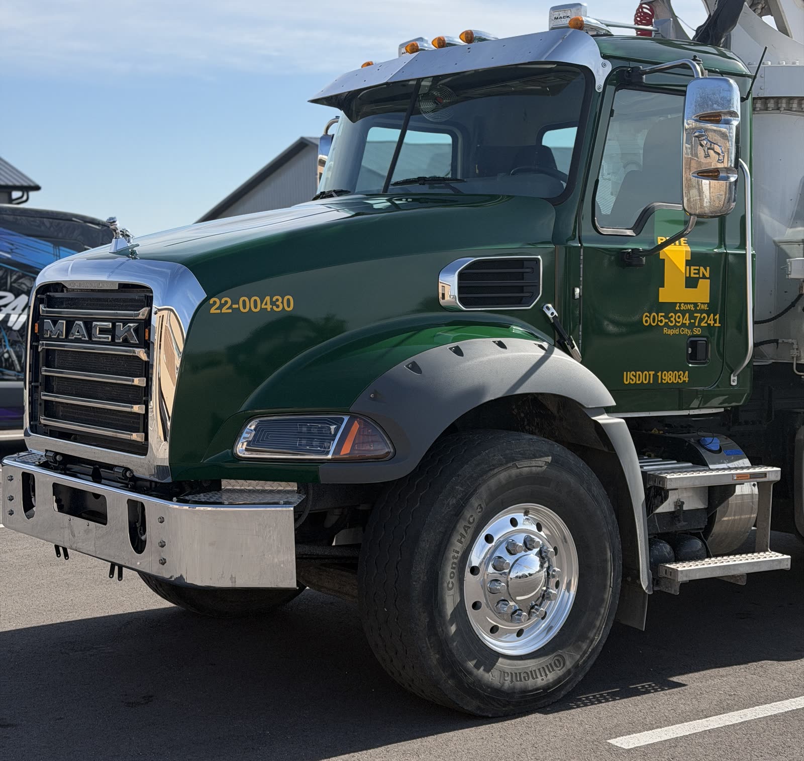 Green Mack work-truck cab with yellow business lettering, chrome grille and bumper, viewed from the front and side