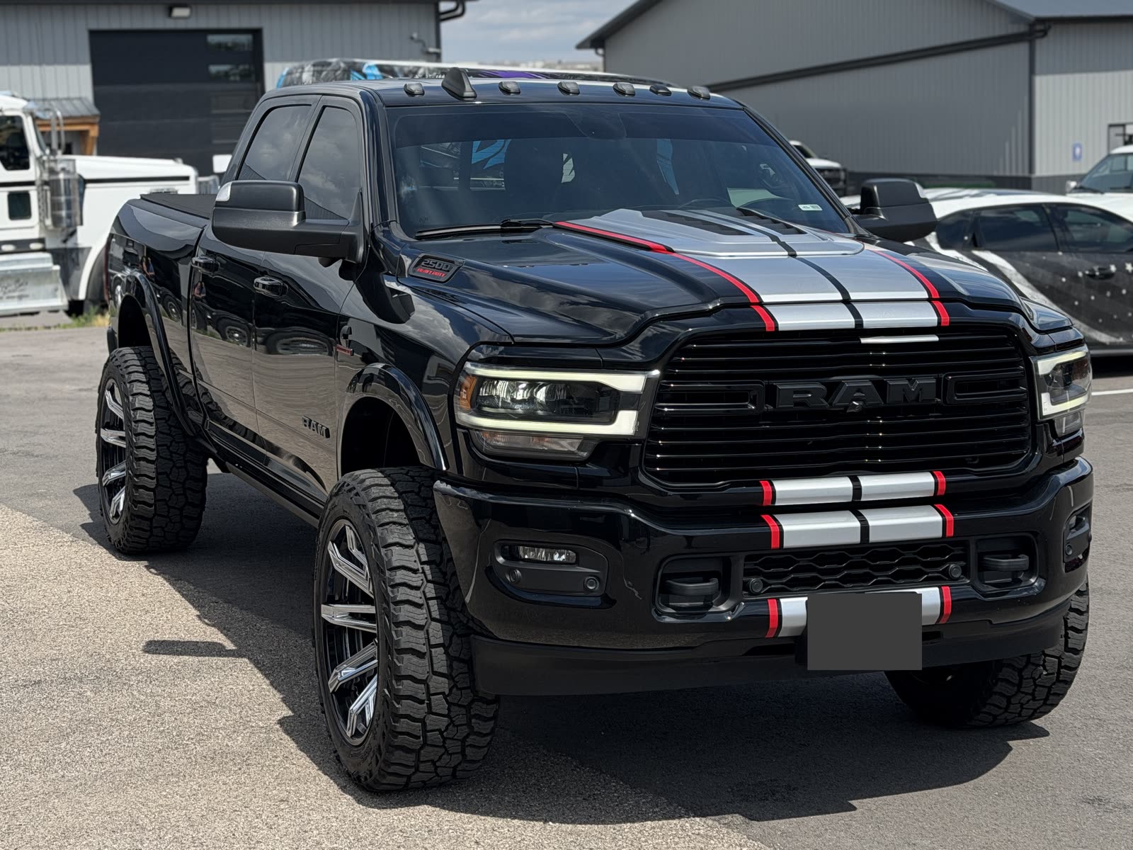 Black Ram pickup with silver hood and front bumper stripes edged in red, parked outside the shop.